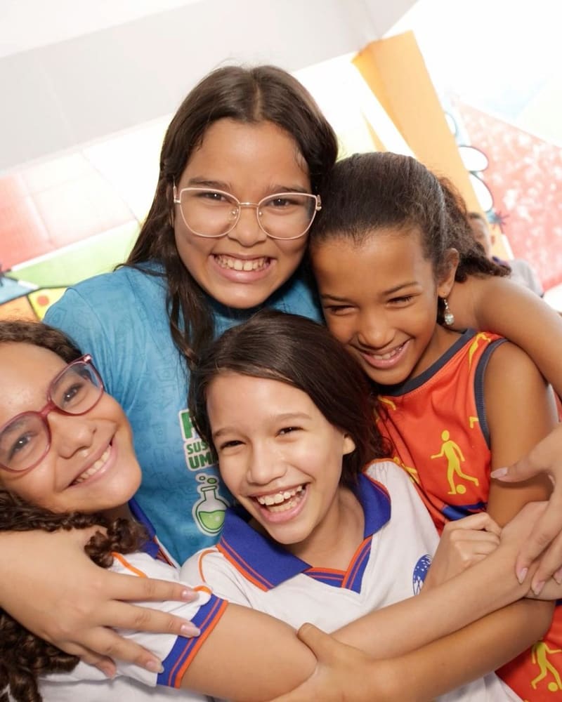 Professora abraçada com quatro alunas, todas rindo