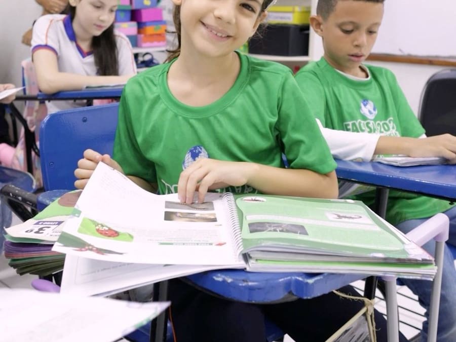 Aluna do Fundamental I sorrindo com o livro aberto na carteira