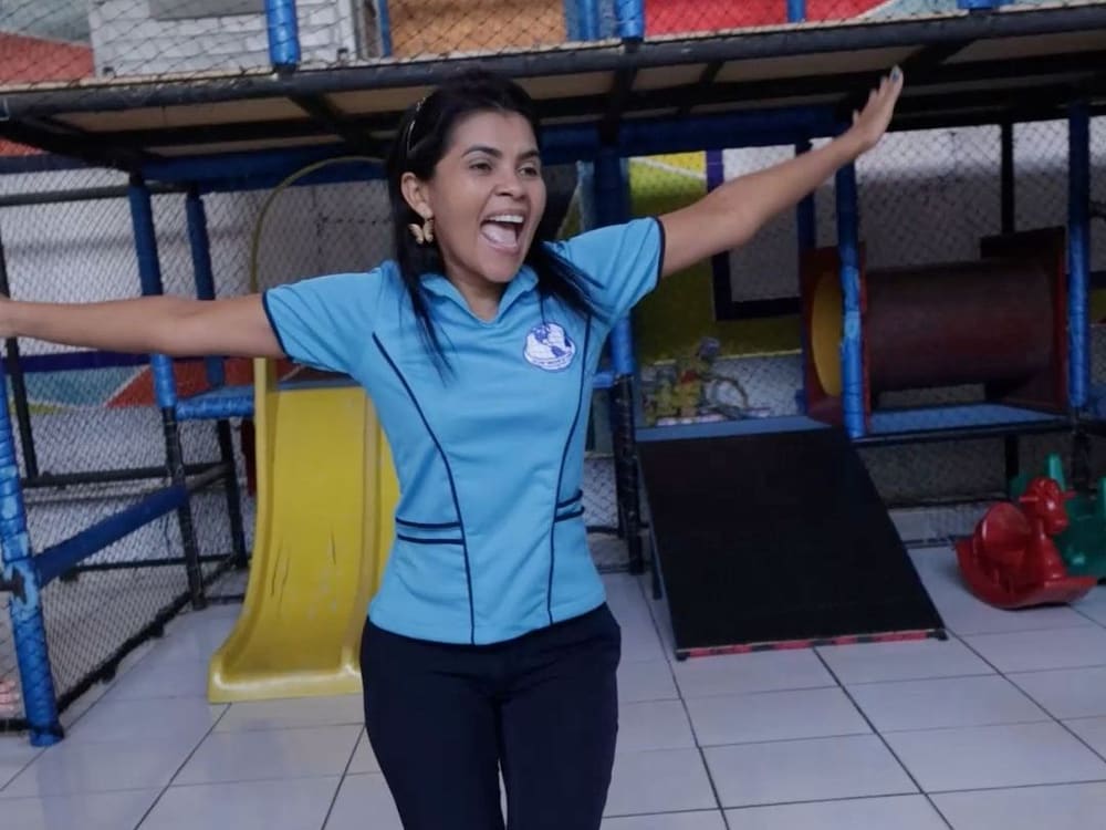 Professora de braços abertos no parquinho coberto da área do Infantil