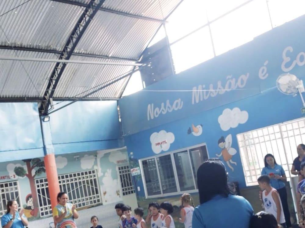 Pátio coberto do Infantil, com as crianças em fila e o mural “Nossa missão é educar”